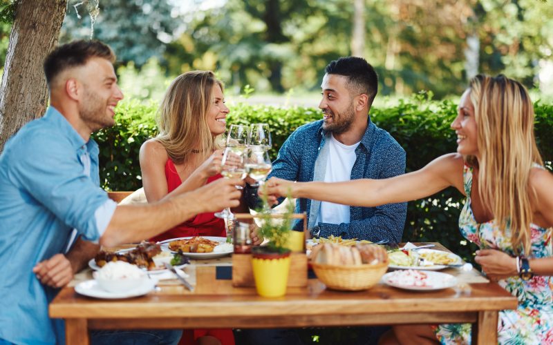 Group of young happy people having lunch at a restaurant during a sunny summer day and toast with wine